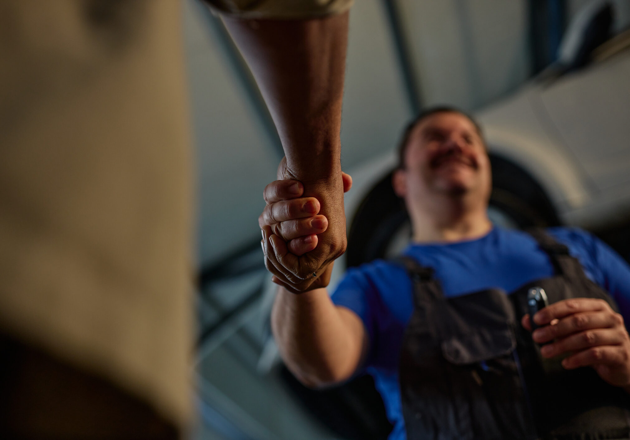 Customer and mechanic shake hands in a busy auto repair shop after a successful car repair, conveying trust, professionalism and satisfaction in a warm, low-light garage environment.